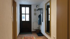 Un pasillo con una puerta, un radiador, un espejo y una alfombra.