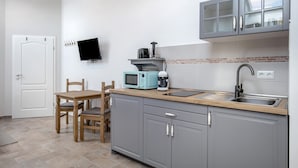 Una cocina con armarios grises, una mesa de madera, un microondas, una cafetera y un televisor montado en la pared.