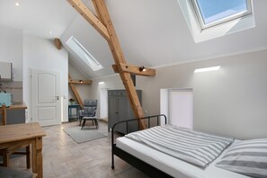 A bedroom with a skylight, a bed, a desk, and a chair.