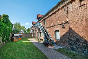 Un bâtiment en briques avec un escalier menant à un étage supérieur, un espace extérieur couvert et un chemin pavé.