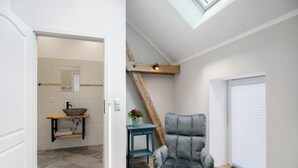 Un interior moderno con un baño, una silla gris, una viga de madera y una ventana con persianas.