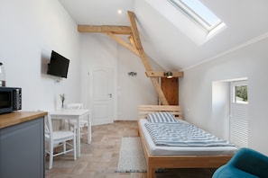 Une chambre avec un plafond en pente, un lit, un téléviseur fixé au mur, un bureau avec une chaise et une fenêtre.