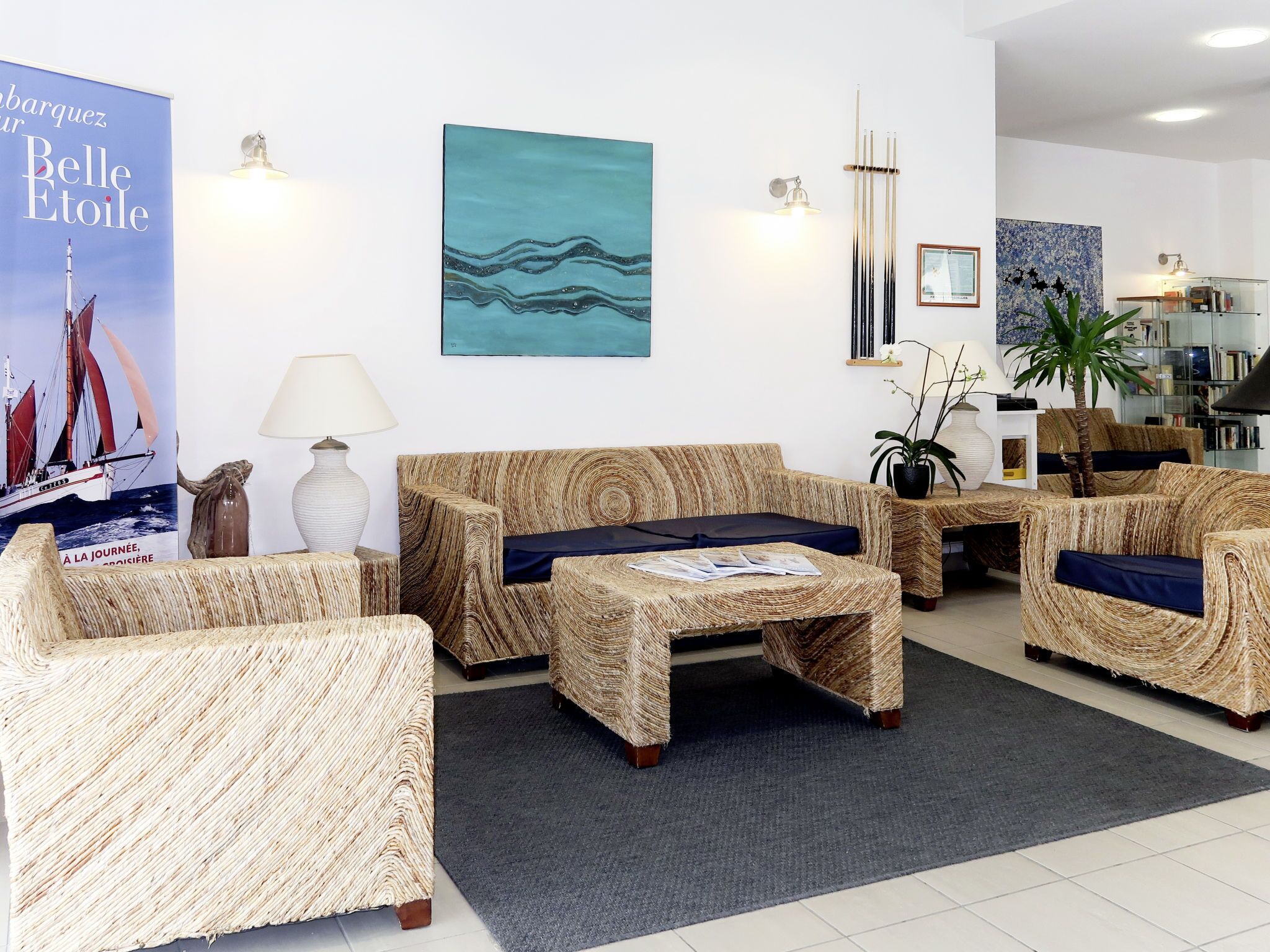Una sala de estar moderna con muebles de mimbre, un cuadro abstracto azul y un cartel de un barco a vela.