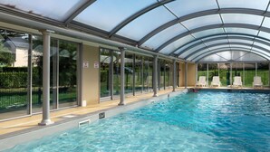 Una piscina interior con agua cristalina, rodeada de paredes y columnas de vidrio, y un techo cubierto.