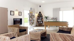 Una sala de estar acogedora con mobiliario de mimbre, mesa de billar, estantería y chimenea.