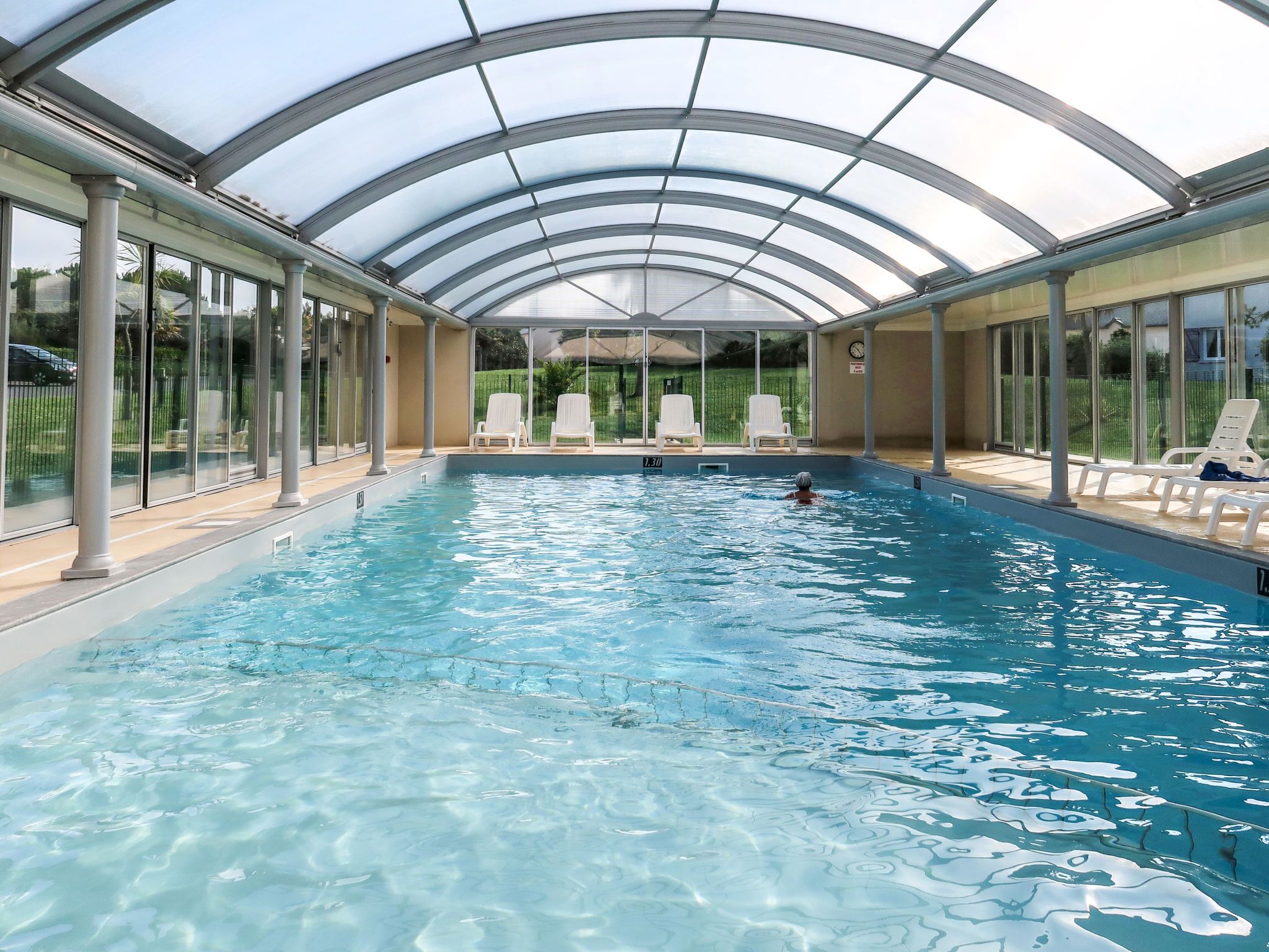 An indoor swimming pool with clear water, surrounded by glass walls and white lounge chairs.