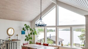 A dining area with a wooden table and chairs, large windows with a view of a lake, and a chandelier.