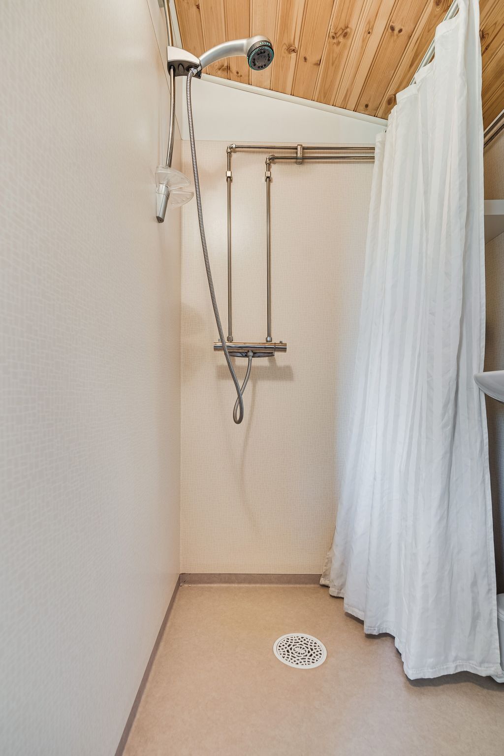 A shower area with a wooden ceiling, a white shower curtain, and a metal showerhead.