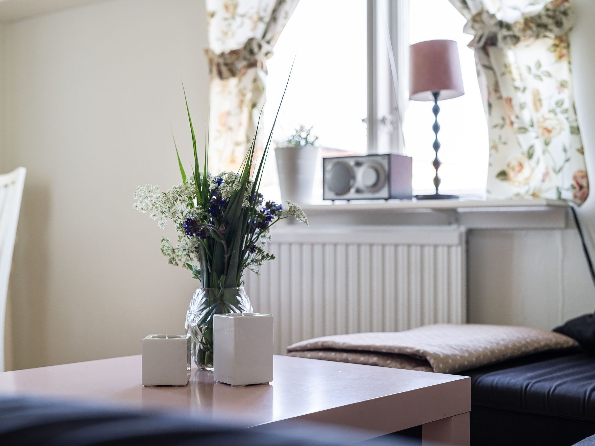 A room with a table, a vase with flowers, a lamp, and a radiator.