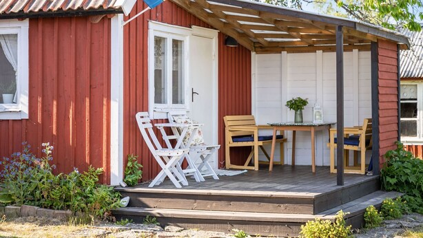 A red wooden house with a covered porch, a white door, and a small table with chairs.