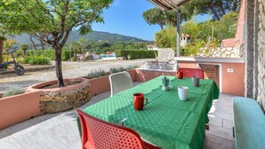 Un espace extérieur abrité, avec une table et des chaises, un mur en pierre et une vue sur le paysage environnant.