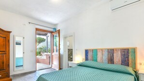 Une chambre à coucher comprenant un lit, une armoire en bois, une salle de bain et une porte donnant sur un espace extérieur.