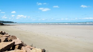 Una playa con cielos despejados, mar tranquilo y formaciones rocosas.