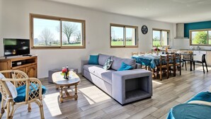 Un amplio espacio de sala con un sofá, una mesa de centro y un televisor. Hay un comedor con una mesa y sillas.