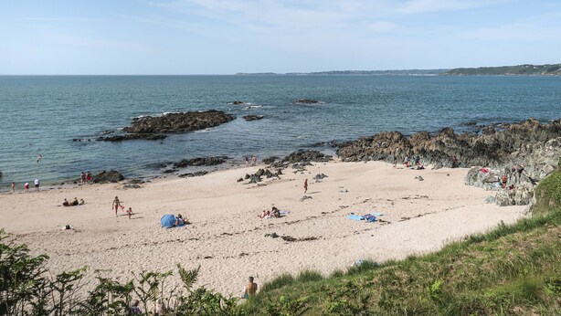 Een strand met rotsachtige rotsformaties en rustig water.