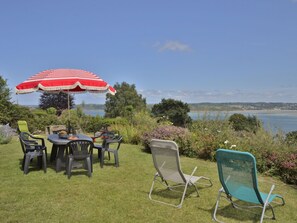 Un patio con mesa y sillas, una sombrilla y vista al mar.