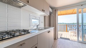 Een moderne keuken met een gasfornuis, een gootsteen en uitzicht op een houten terras en een waterpartij.