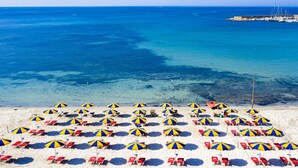A beach with numerous blue and yellow striped umbrellas and red lounge chairs arranged in rows. - Camping Village Laguna Blu by Interhome (Alghero)
