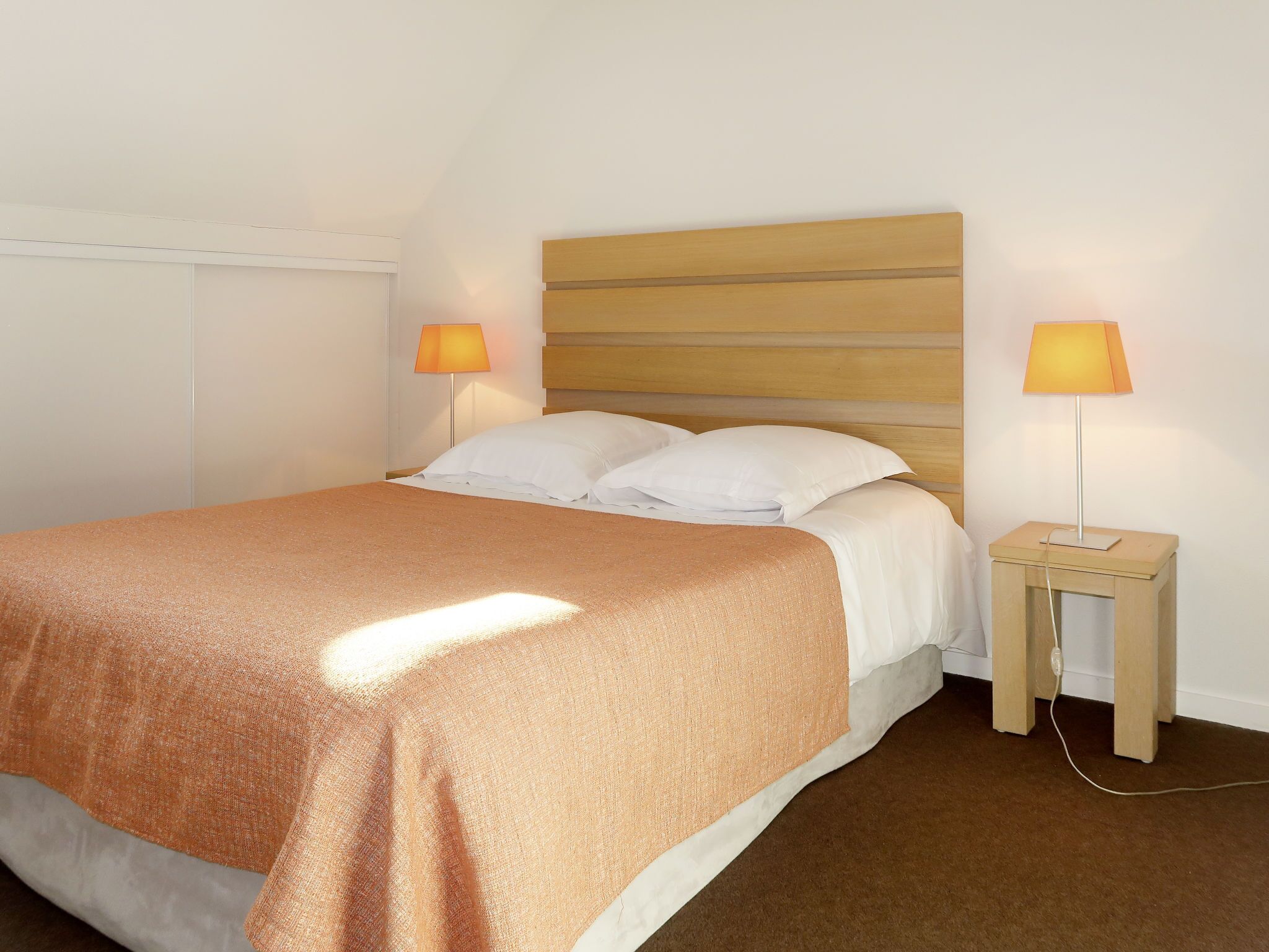 A neatly made bed with a wooden headboard, two bedside lamps, and a small wooden nightstand.