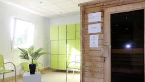A room with green lockers, a potted plant, and a wooden door with informational signs. - Cap Green 24 by Interhome (Frehel/Cap Frehel)