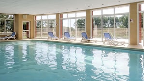 An indoor swimming pool with clear blue water, surrounded by white lounge chairs and large windows. - Cap Green 24 by Interhome (Frehel/Cap Frehel)