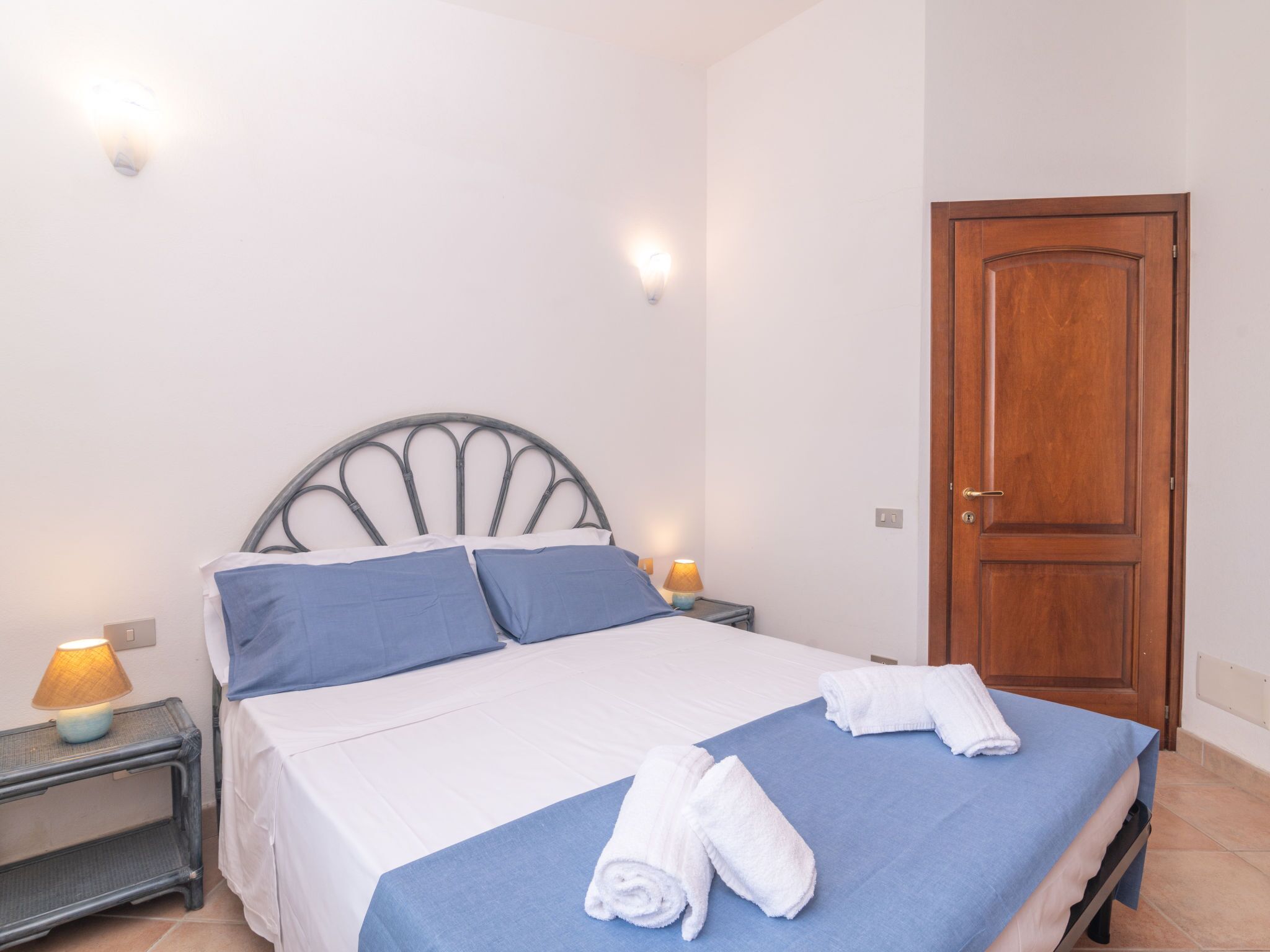 A neatly made bed with blue and white linens, two bedside lamps, and a wooden door.