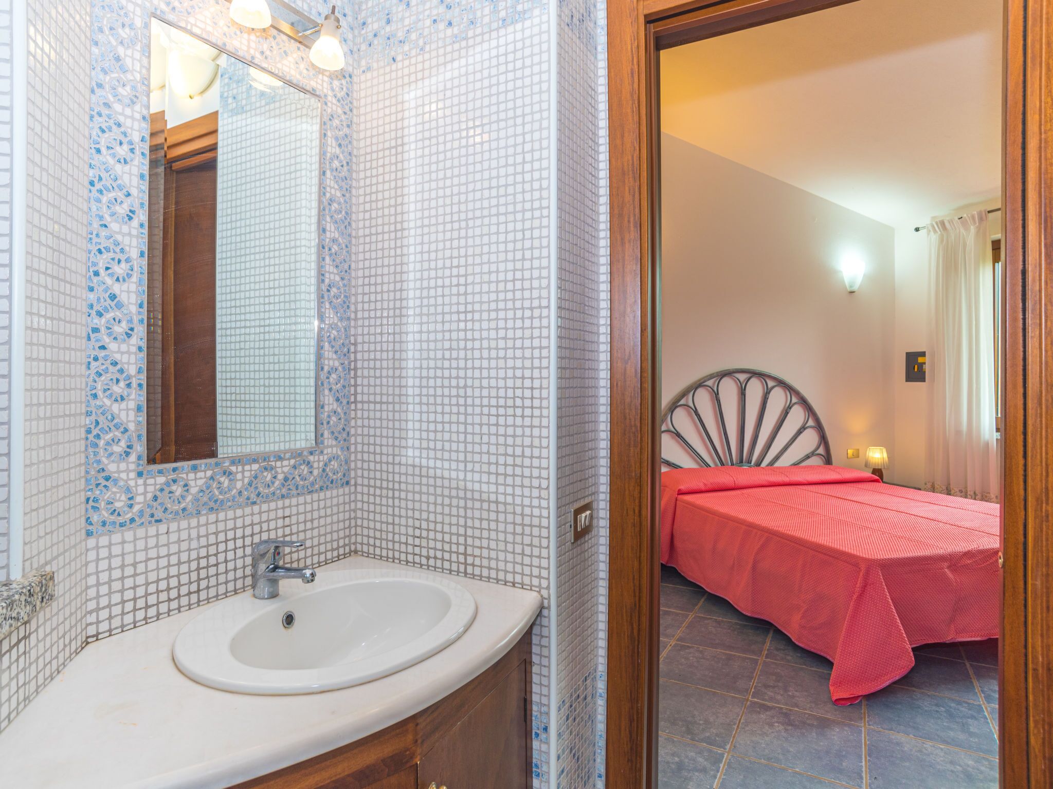 Une salle de bain avec un lavabo blanc, un miroir et des murs recouverts de mosaïques.