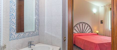 Une salle de bain avec un lavabo blanc, un miroir et des murs recouverts de mosaïques.