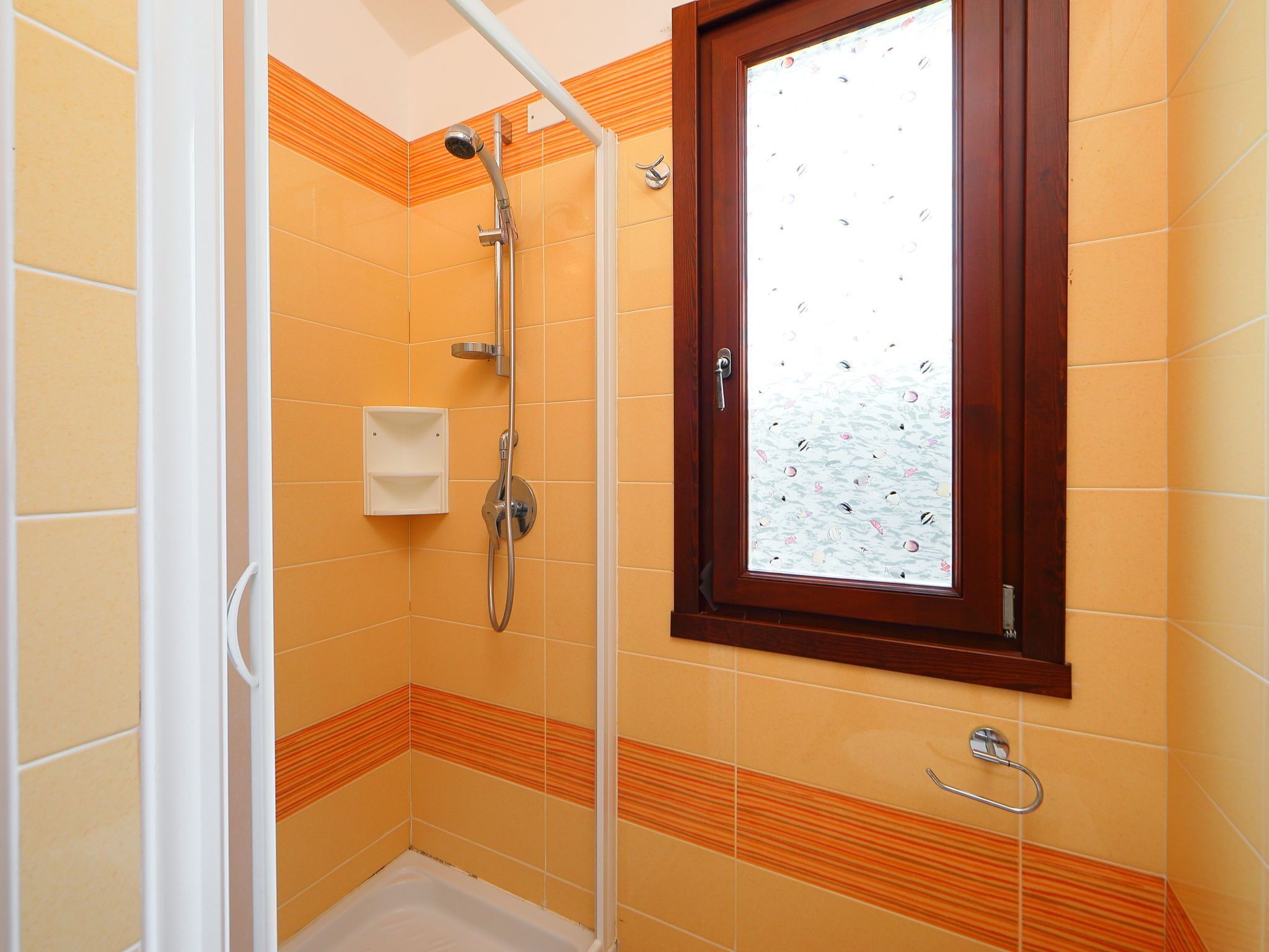 A small bathroom with orange tiles, a shower, a window with a decorative pattern, and a towel rack.