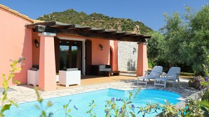 A poolside area with lounge chairs, a covered seating area, and a view of a mountainous landscape. - Ville San Pietro (REI352) by Interhome (Costa Rei)