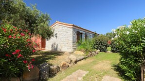 A stone building with a tiled roof, surrounded by a garden with various plants and a stone pathway. - Ville San Pietro (REI352) by Interhome (Costa Rei)