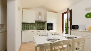 A kitchen with white cabinets, a green tiled backsplash, a microwave, and a dining table set for four. - Ville San Pietro (REI352) by Interhome (Costa Rei)