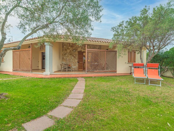 A house with a stone facade, a tiled roof, and a covered patio area with outdoor furniture.