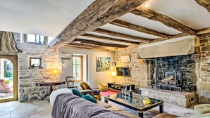 Un intérieur rustique en pierre, avec un plafond en bois, une cheminée et un coin salon confortable comprenant un canapé et des fauteuils.