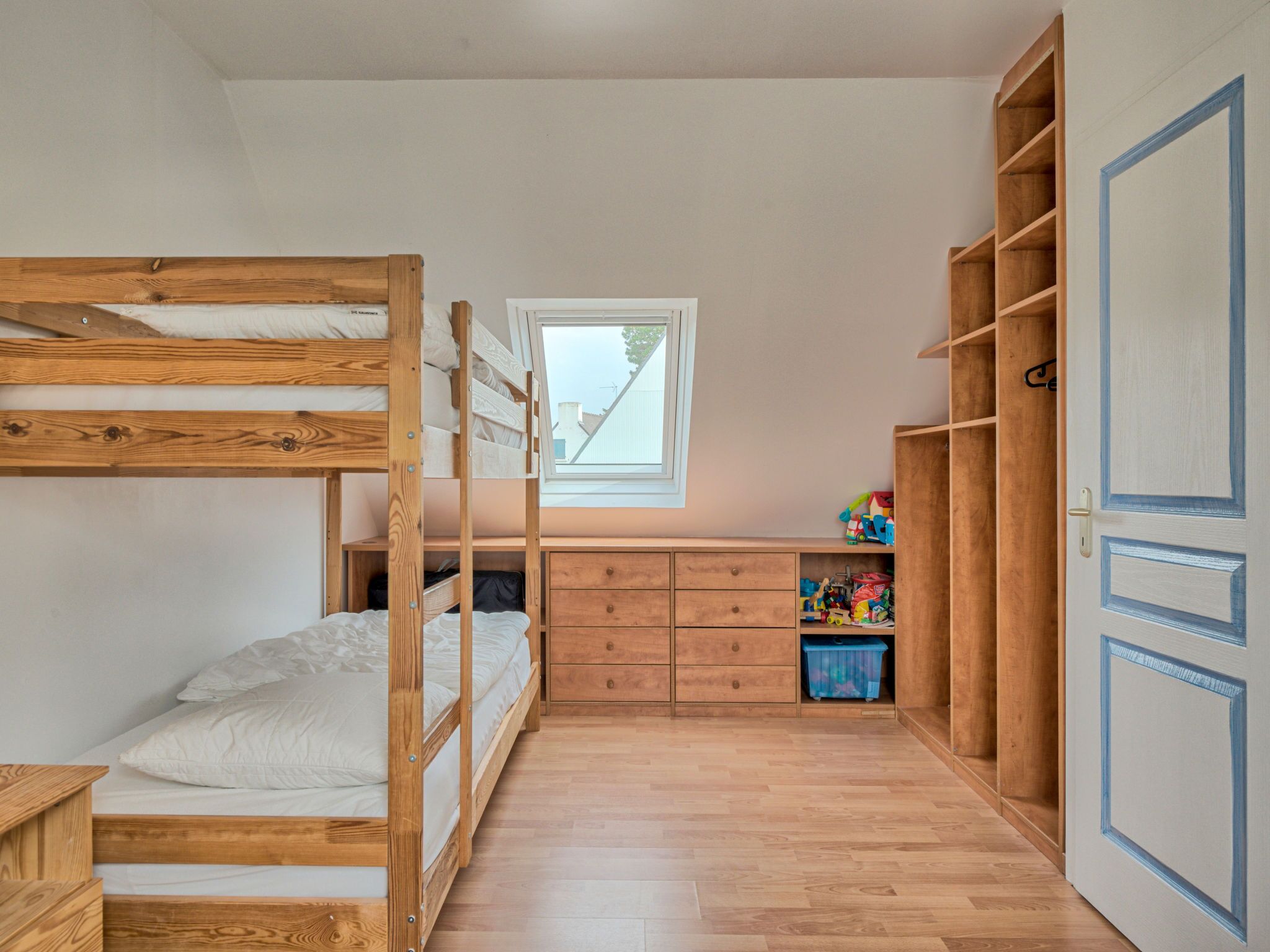 A bunk bed room with a window, wooden desk, and built-in shelves.