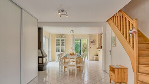 Un vaste espace dédié à la salle à manger, avec une grande table et des chaises, un escalier en bois et une vue sur l’extérieur.
