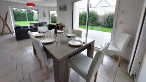 A dining area with a table set for four, surrounded by chairs, with a view of a garden through large sliding doors. - Golf de Bretagne by Interhome (Sarzeau)