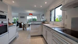 A modern kitchen with white cabinets, a large window, and a dining area with chairs and a table. - Golf de Bretagne by Interhome (Sarzeau)