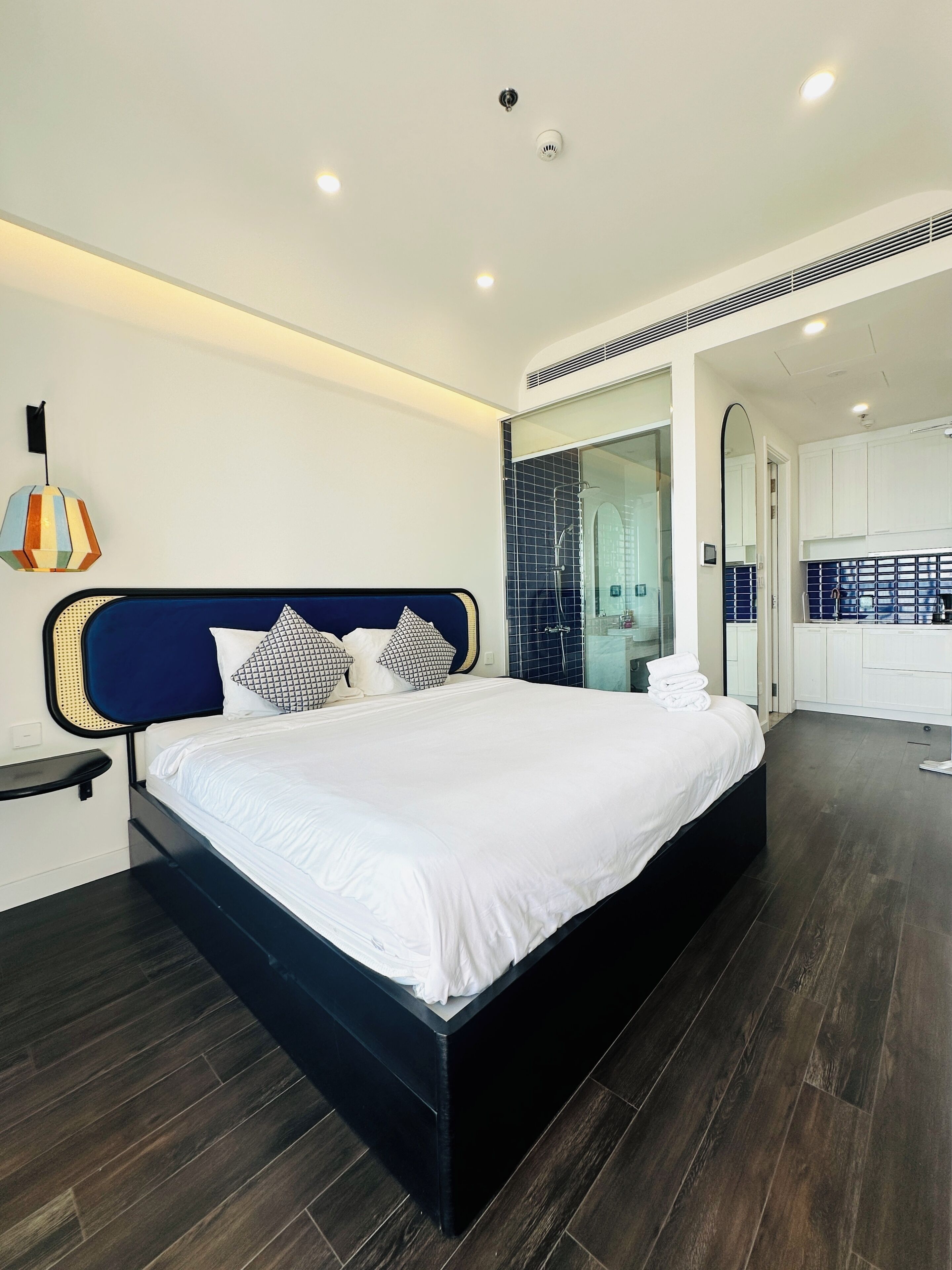 A modern bedroom with a large bed, a bedside table, a mirror, and a bathroom visible through an open door.