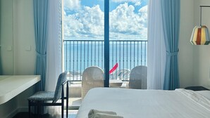 Hotelkamer met een groot bed, een stoel, een klein tafeltje en een balkon met uitzicht op de lucht en wolken.