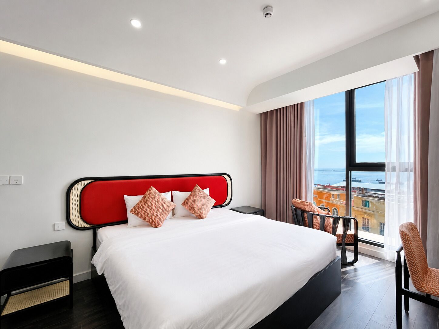 Ein modernes Hotelzimmer mit einem großen Bett, Blick auf die Stadt und einem Sitzplatz auf dem Balkon.