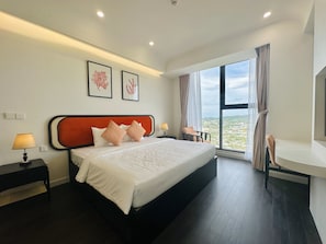 A modern hotel room with a large bed, a nightstand with a lamp, a chair, and a large window offering a city view.