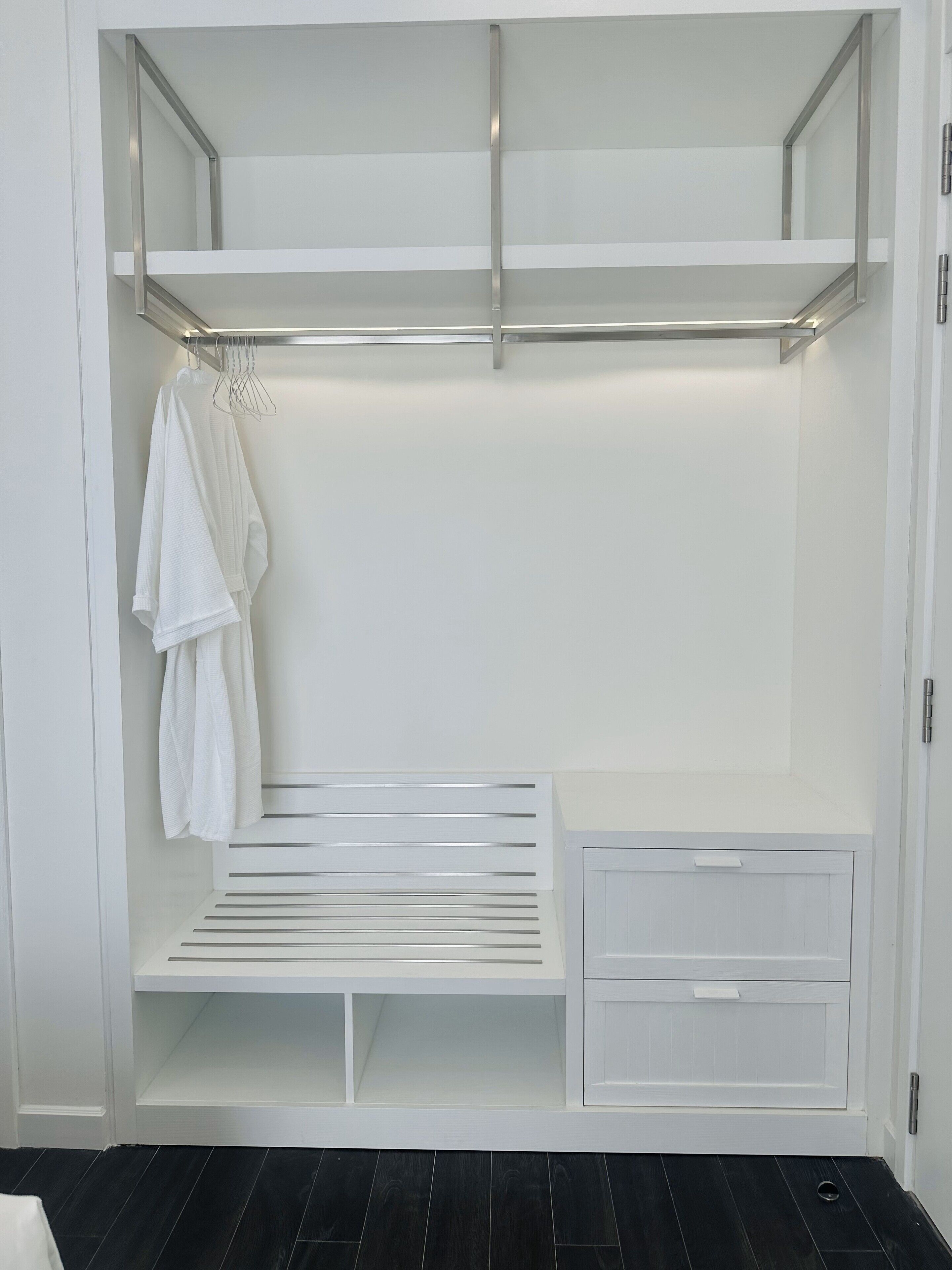 Un dressing accessible sans porte, doté d’une armoire à miroir, d’une tringle à vêtements et d’un banc intégré.