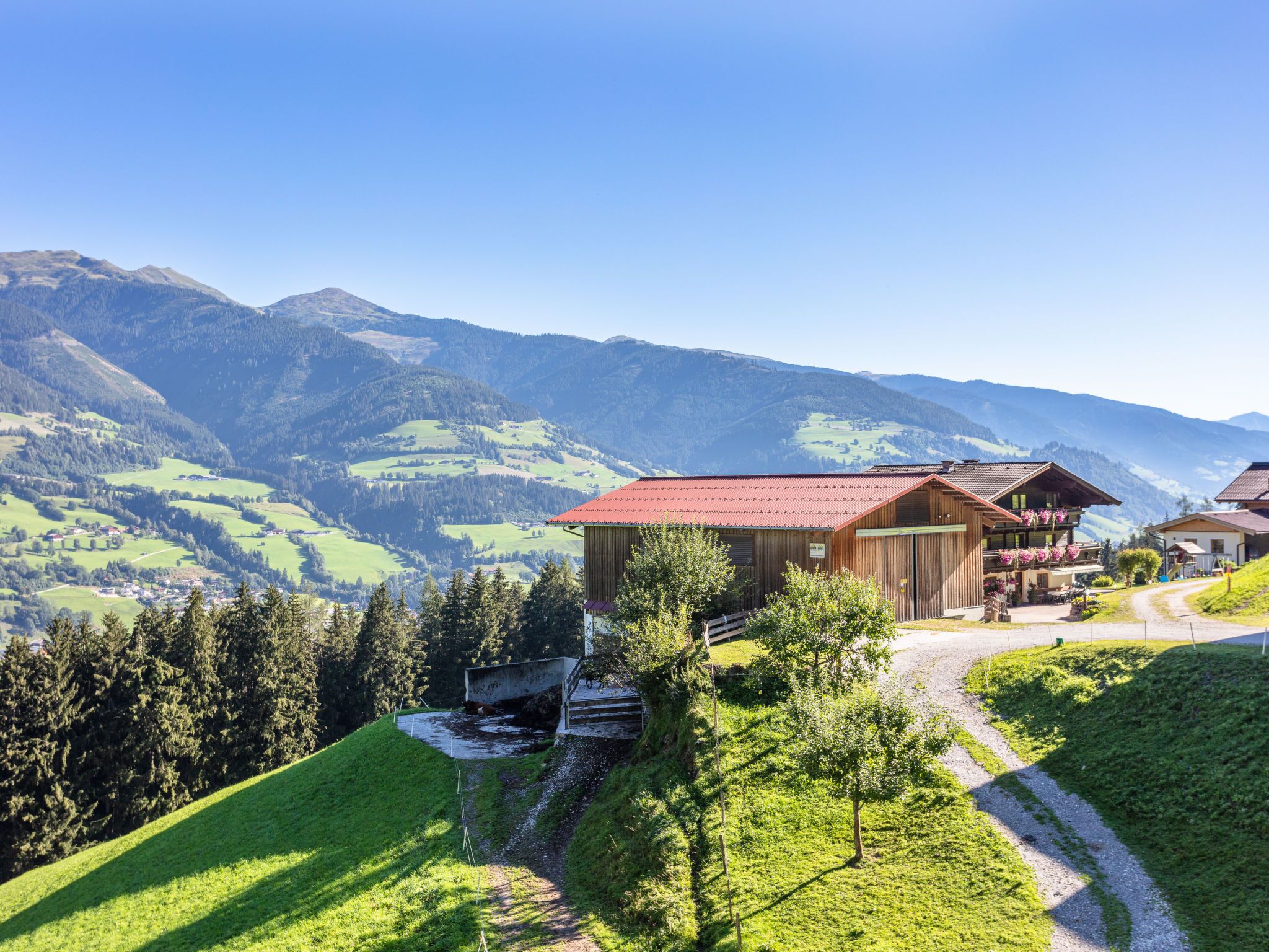 A mountain lodge with a red roof, surrounded by lush green hills and mountains in the background.