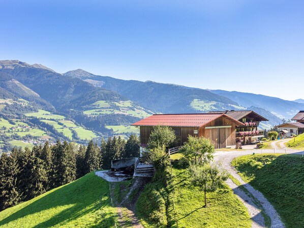 A mountain lodge with a red roof, surrounded by lush green hills and mountains in the background.
