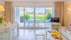 Een ruime kamer met een eethoek, een bank met televisie, en een balkon met uitzicht op de tuin.