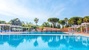 A clear blue pool with lounge chairs and umbrellas, surrounded by palm trees and a clear sky.
