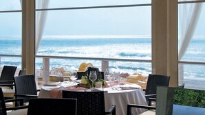 A dining area with a table set for two, overlooking a beach with waves.