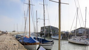 Een jachthaven met verschillende zeilboten afgemeerd, een pad van stenen en een gebouw met de tekst 'QUICK SILVER' op de achtergrond.