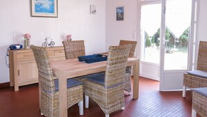 Een eetruimte met een houten tafel, rieten stoelen, een fiets en een radio op een kast.